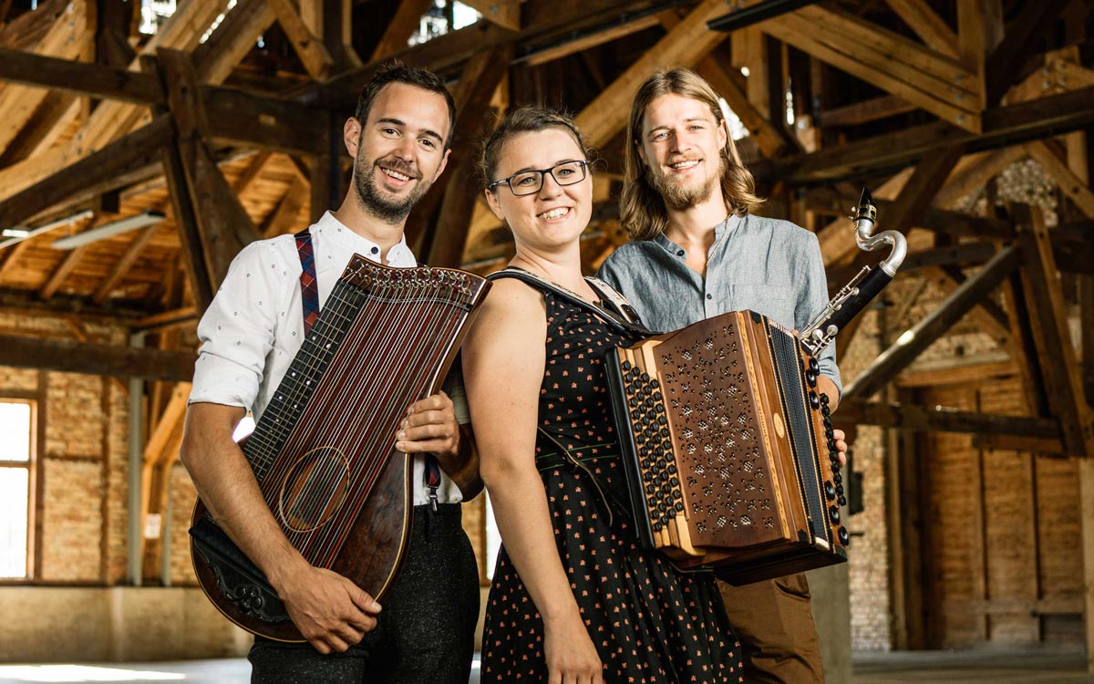 Trio Tschejefem mit Instrumenten in einem Stadl mit alten Holzbalken