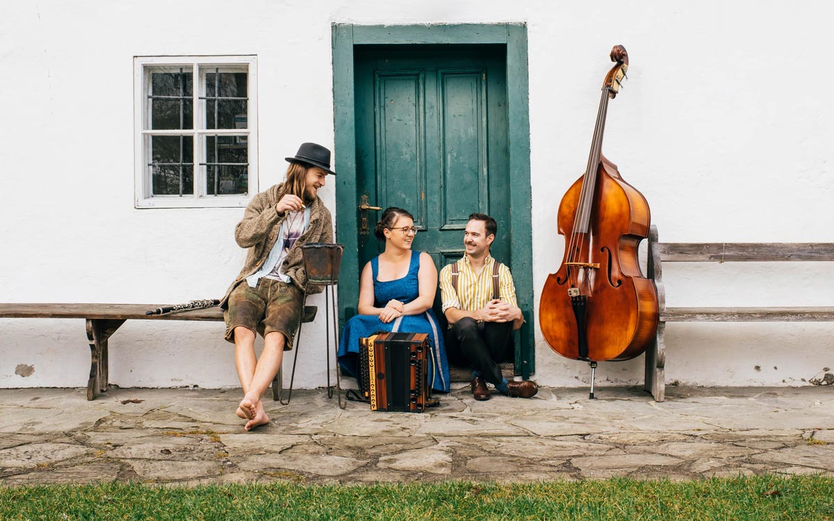 Trio Tschejefem mit Instrumenten vor einem alten Bauernhaus